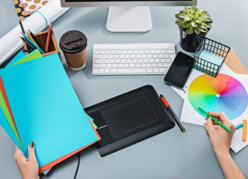 The gray desk with laptop, notepad with blank sheet, pot of flower, stylus and tablet for retouching